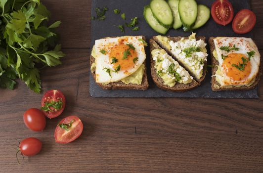 Avocado Toast. Healthy Breakfast. Top View. Homemade Sandwich With Avocado And Fried Eggs, Cherry Tomato And Cucumbers On A Wooden Background. Dark Food Photography