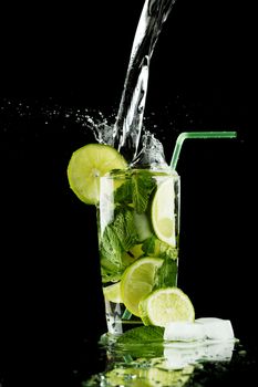 Pouring fresh mojito cocktail in glass isolated on black background