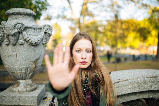 Attractive young woman in park is displeased and making a stop sign with her hands