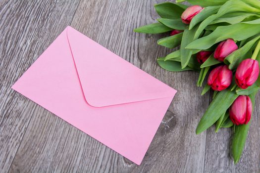 Pink envelope with tulips on a wooden table