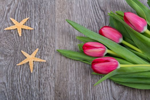 Starfishes and red tulips on a wooden table