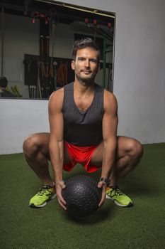 Young man in squat position, holding a black weighted ball