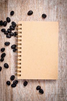 Blank vintage notebook with coffee beans on wooden background, Top view.
