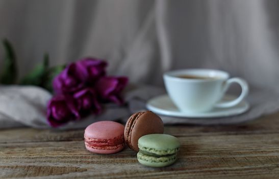 Macaroon biscuits on a wooden background with flowers and a cup of coffee