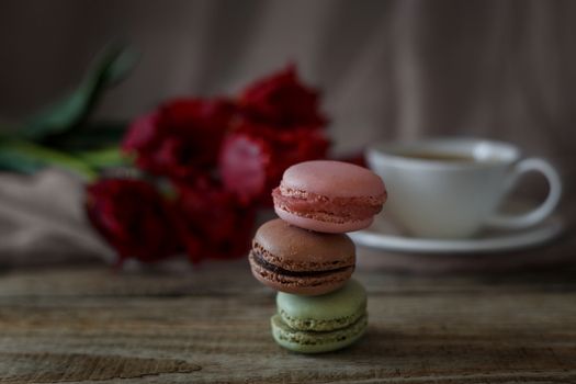 Macaroon biscuits on a wooden background with flowers and a cup of coffee