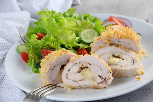 Sliced baked until golden, crispy crust chicken roll in breadcrumbs with Parmesan cheese, stuffed with cheese with herbs and garnish of vegetables.