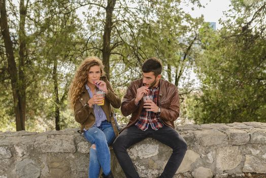 Young modern lovers taking a rest after a long walk and refreshing with orange juice