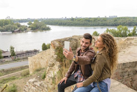 Handsome man is taking a selfie photo with his attractive long haired girlfriend outdoors
