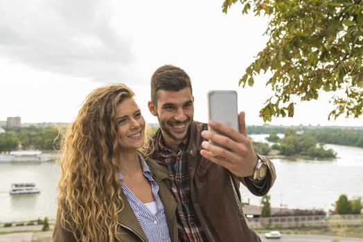 Happy and young attractive lovers enjoying the time near the river bank by taking a selfie photos