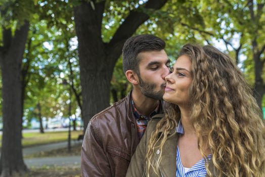 Modern guy with beard kissing his girlfriend in the public park