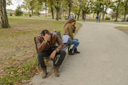 Attractive and modern lovers feeling disappointed after breaking up long relationship. Sitting on the bench in public park.