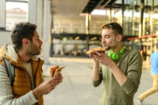 Two young hipsters are enjoying a snack in the city street