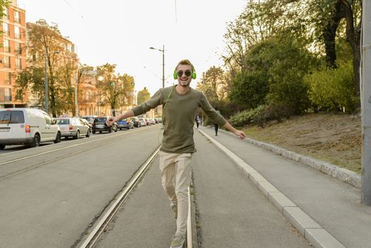 Young handsome hipster is walking and balancing on the tramway rails in the city