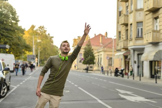 Young man with green headphones stopping taxi in the city street