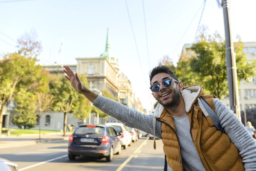 Handsome hipster with orange jacket and sunglasses stopping taxi in the city street