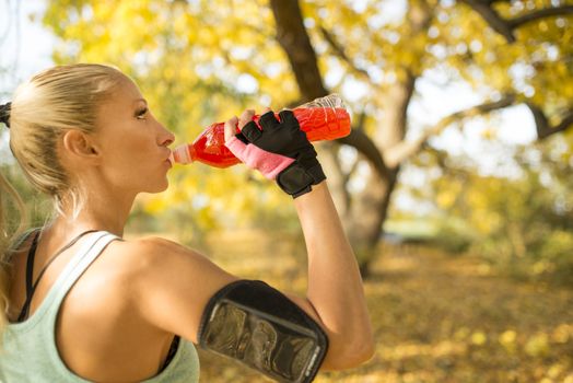 Sexy blonde sportswoman is refreshing with cold drink after hard exercise