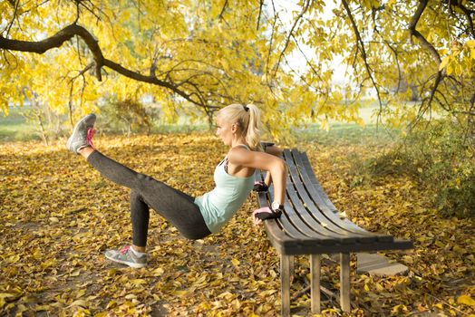 Young sportswoman stretching her legs at wooden bench in public park