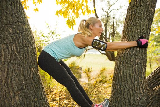 Attractive female athlete climbing on the tree in the public park and exercising. Healthy lifestyle concept.