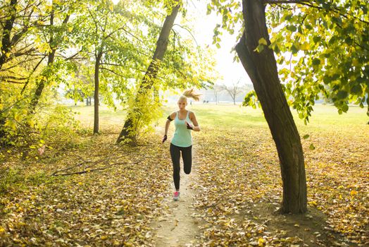Attractive young sporty woman jogging in the park covered with leaves between the trees. Healthy lifestyle concept.
