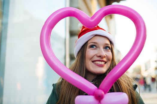 Attractive young woman with santa claus hat standing in the street with heart shaped balloon