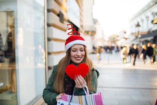 Young woman with santa claus hat holding a heart shape in the street
