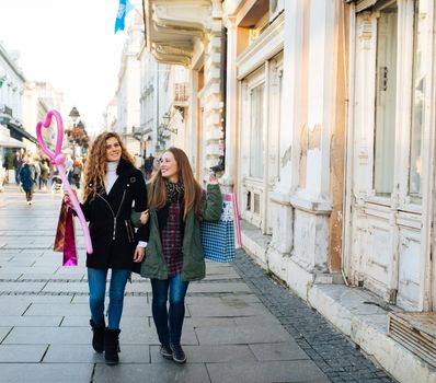 Two attractive young women is satisfied with shopping and walking down the street