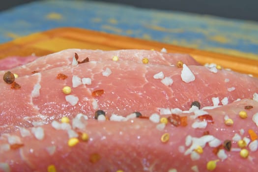 Raw pork loin chops on a cutting board with salt, pepper on brown cutting board. Slices of pork steaks. Pork chops ready to fry. Selective focus. 