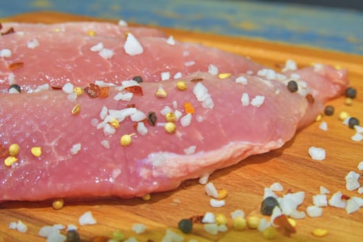 Raw pork loin chops on a cutting board with salt, pepper on brown cutting board.