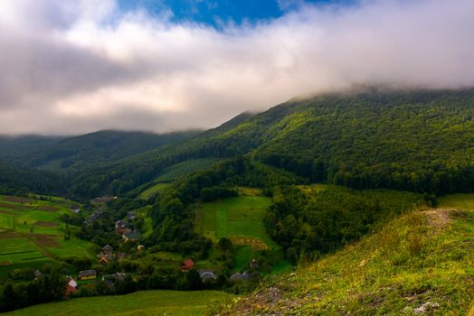 small Carpathian village in mountains. beautiful landscape with forested hills and agricultural fields on a cloudy morning