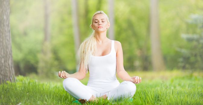 Young girl doing lotus yoga exercise in spring park