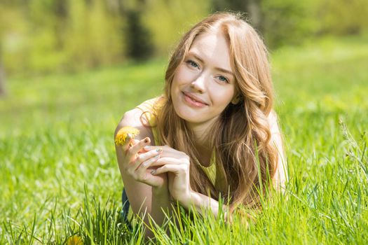 Redhead or blonde romantic beautiful young woman laying on grass in park