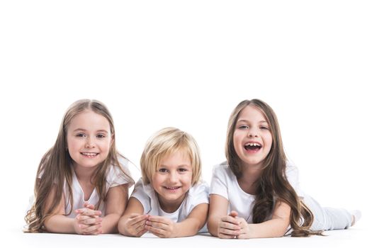 Happy smiling three children in white clothes laying on floor isolated on white background