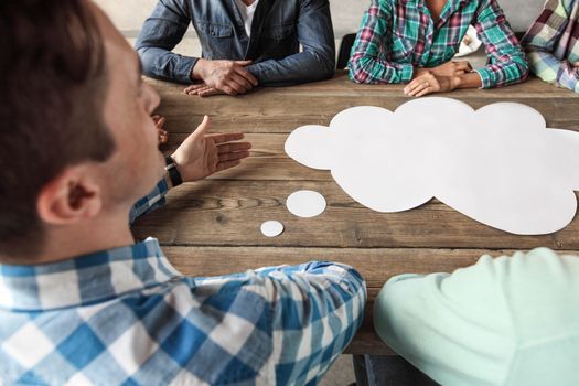 Hipster business teamwork brainstorming planning meeting concept, man tells his opinion, people sitting around the table with white paper shaped like dialog cloud