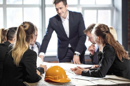 Business people discuss construction blueprint, hardhat on office table
