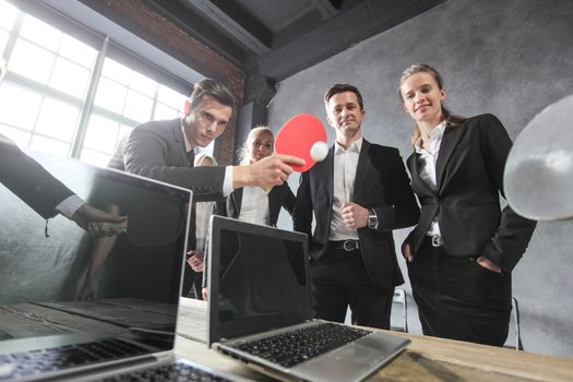 Business people play ping pong on office table with laptops