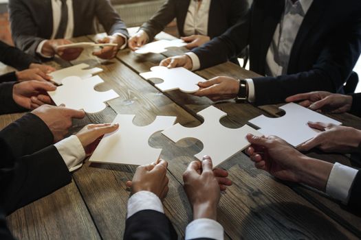 Business people and puzzle on wooden table, teamwork concept
