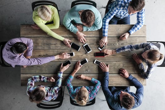 Team of business people in casual clothes sitting around the table, taking their mobile phones, top view