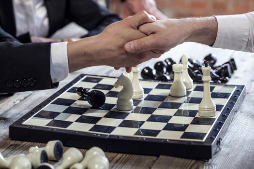 Business people shaking hands over chessboard after the game