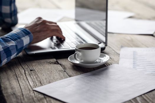 Man working on a laptop on a rustic wooden table, hands close up