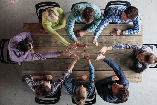 Modern business meeting concept, people in casual clothes sitting around wooden table giving high five