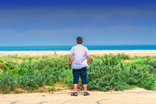 Man stands on the beach and looks out to sea
