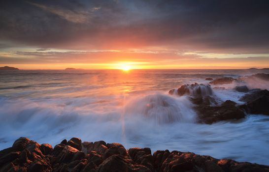 Sunrise skies and ocean waves crash over rocks.  Port Stephens Australia