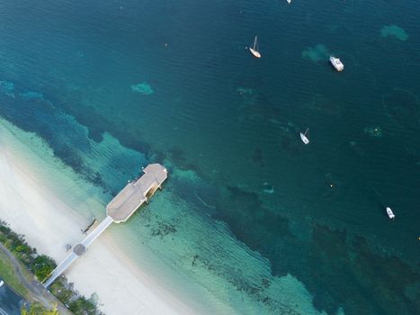 Aerial veiw of the Shoal Bay jetty in Port Stephens, photographed in early morning light.  Yachts and boats are moored just offshore and a couple of fisherman  cast their lines from the jetty.