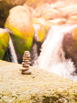 Balancing stone pyramid of pebbles with river waterfall on background.
