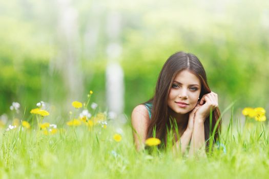 Young beautiful woman resting on fresh green grass with flowers