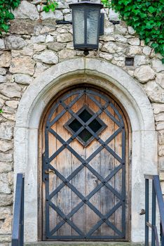 a wooden door with a metal grille in a medieval building, a lantern above the entrance