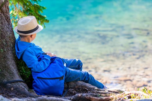 A boy of 8 years with a backpack resting by the lake in the Tatras