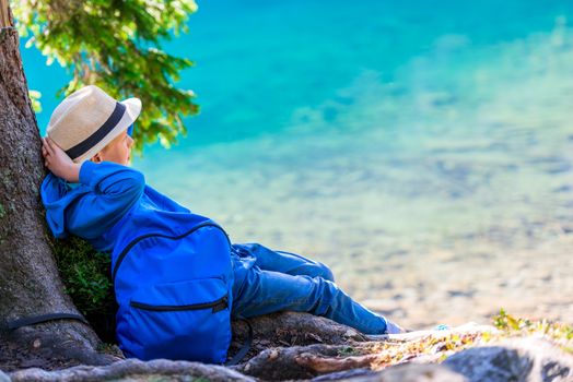 Boy tired traveler with a backpack resting at a lake in the Tatra Mountains