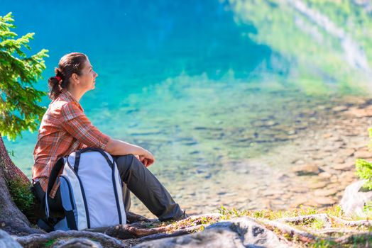 traveler with a backpack sits by the lake Morskie Oko in the Tatra Mountains and admires