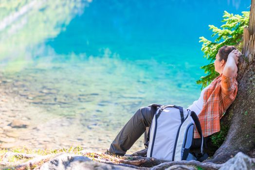 woman with a backpack relaxes and rests by the lake in the mountains